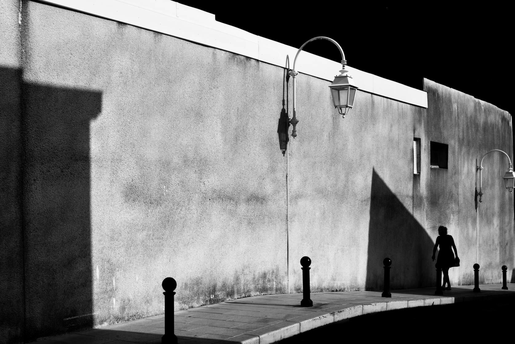 The Edge of Light Street photograph of a lone pedestrian walking through strong light and geometric shadows in Arcachon, France by Franck Prevot