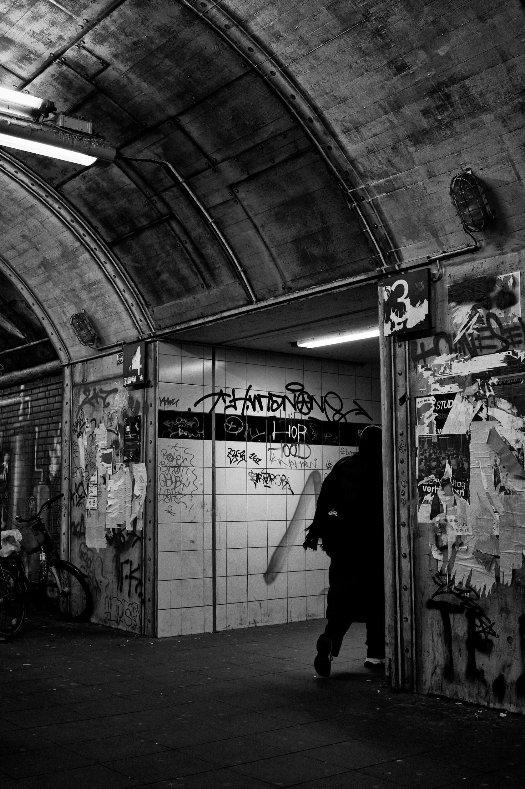 Cologne Noir 11 Black and white street photograph of a lone figure in a graffiti-covered underground passage in Cologne, from the Cologne Noir series, part of the Cologne City Museum collection, by Franck Prevot