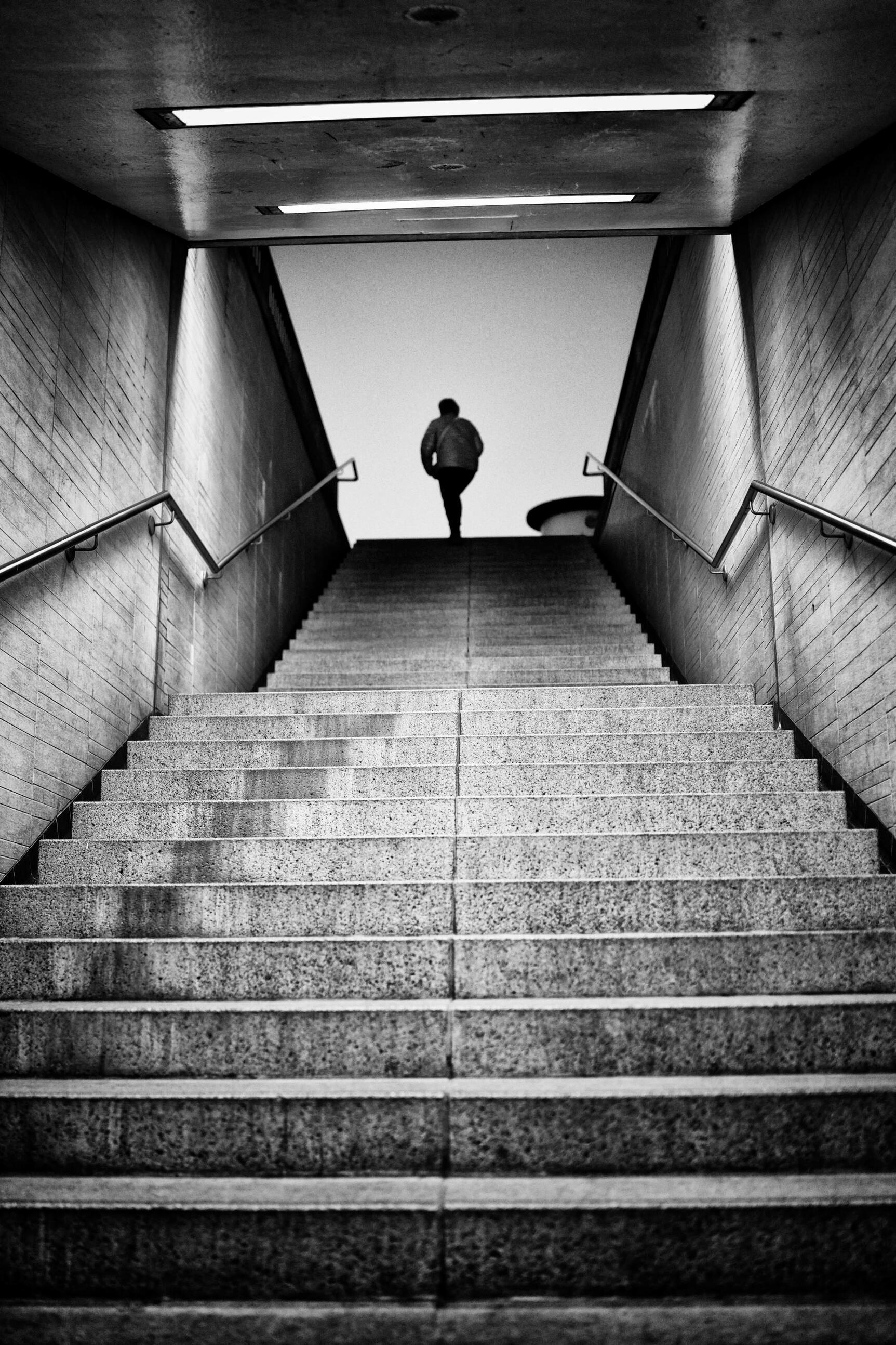 Cologne Noir 12 Black-and-white street photograph of a solitary figure at the top of a symmetrical staircase in Cologne, from the museum-collected Cologne Noir series by Franck Prevot.